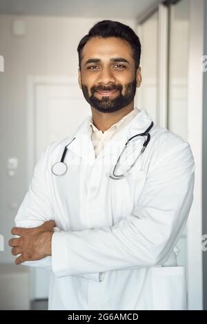 Vertical portrait of smiling young indian male doctor in medical robe uniform Stock Photo