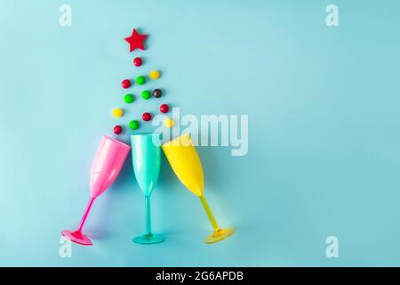 New Year and Merry Christmas party concept. Top view flat lay Christmas tree shape made from bright plastic champagne glasses, candy drops, red star o Stock Photo