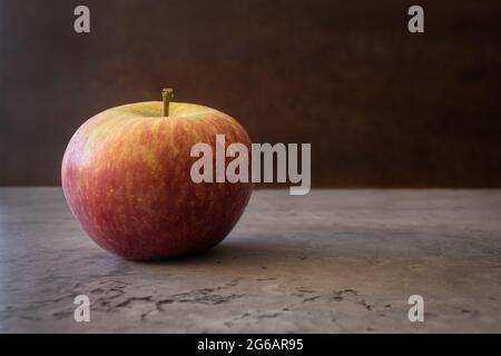 Still life of one fuji apple with left alignment resting on a counter isolated on a dark textured background. Fruit photography with space for text Stock Photo