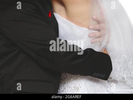 The groom in a black stylish suit hugs the bride tightly in a close-up white dress. Wedding tenderness and affection. Stock Photo