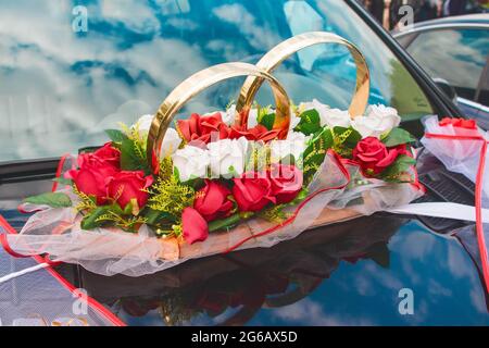 Wedding decoration of the car in the form of rings, artificial colors of red and white roses on the hood of the car. Stock Photo