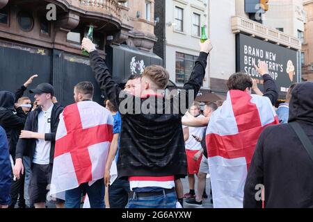 England football fans gather in the West End. A man flanked by two others wearing St George's flag holds up two bottles of beer. Stock Photo