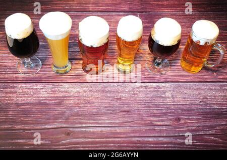 Six glasses of different types of beer are in a row on a wooden table. View from above. Stock Photo