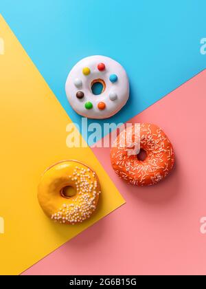 Creative layout made from delicious glazed donuts. Vertical flat lay - donuts or doughnuts on colorful background with copy space. Blue, yellow and pink geometric background. Stock Photo