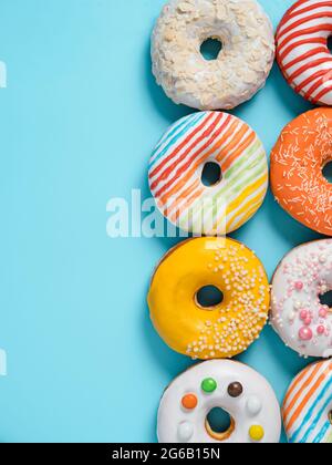 Delicious glazed donuts on blue background. Vertical flat lay - set of different colorful donuts or doughnuts on blue with copy space for text or design. Bright sun light with hard shadows. Stock Photo