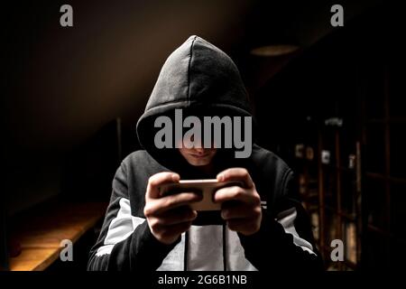 male hacker in the hood using a mobile phone, stealing your personal data Stock Photo