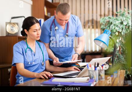 Two focused physicians working with case histories on laptop Stock Photo
