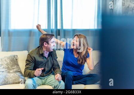 Mature couple celebrating something they are watching on TV. Stock Photo