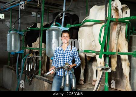 Young milker operating machine milking in livestock barn Stock Photo