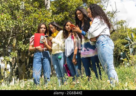 Close-up shot of teenage Latina students with their notebooks, backpacks and cell phones in a park Stock Photo
