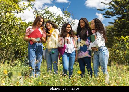 Group of Latina teen girl friends students interacting with their cell phones in a park. Education and lifestyle concept Stock Photo