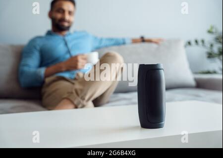 Young man on sofa listening small portable wireless speaker at smart home Stock Photo