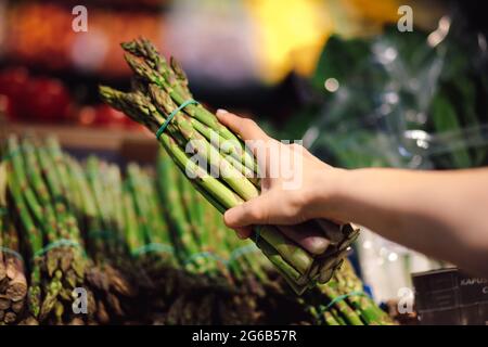 Young woman chooses bunch of fresh asparagus on vegetable display case. Healthy food. The right way of life. Vitamins and fresh vegetables. Enjoying t Stock Photo