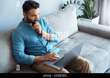 Portrait of thoughtful indian businessman touching chin looking at laptop screen Stock Photo