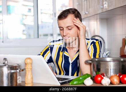 Young man reads a recipe for dishes in a laptop Stock Photo