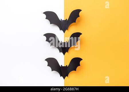Black paper bats on yellow and white background. Creative Halloween concept. Flat lay, top view, copy space - Image Stock Photo
