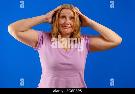Middle age beautiful blonde woman wearing casual purple shirt standing over blue background suffering from headache desperate and stressed because pai Stock Photo