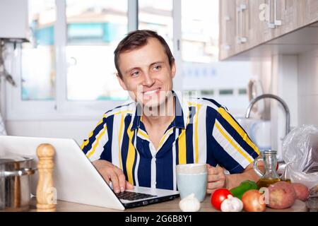 Young man reads a recipe for dishes in a laptop Stock Photo