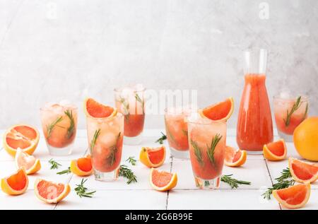 Cold refreshing grapefruit smoothie with rosemary and ice in glasses, grapefruit wedges and rosemary sprigs on the table, home party Stock Photo