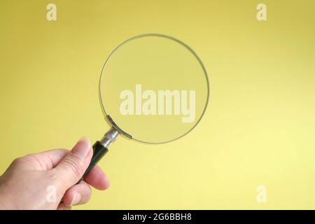 Hand holding magnifying glass. On yellow background. Copy space. Stock Photo