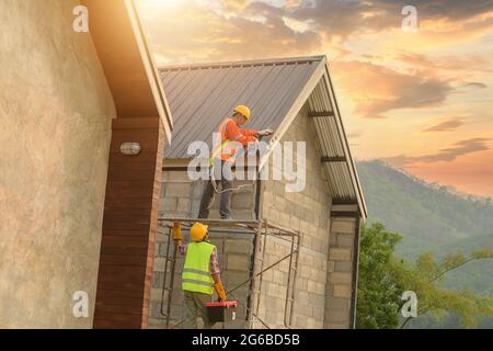 Two construction workers installing metal sheets on roof, Thailand Stock Photo