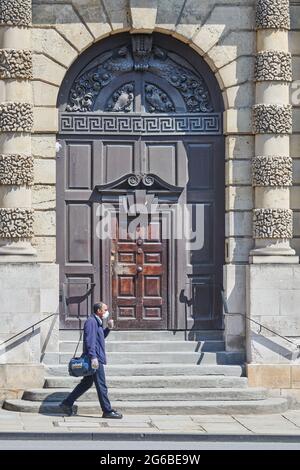 A man wearing a face mask passes the front door of Queen's college, university of Oxford, England, June 2021. Stock Photo