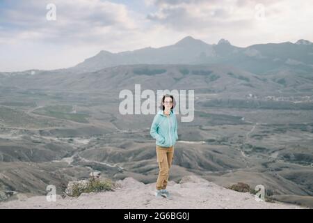 Woman stands against the backdrop of a mountain landscape. Stock Photo