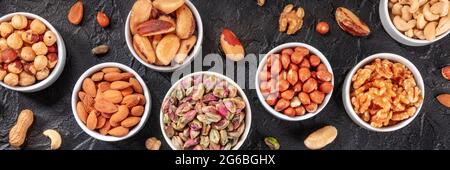 Nuts overhead flat lay panorama with pistachios, almonts, peanuts and many other nuts on a black slate background Stock Photo