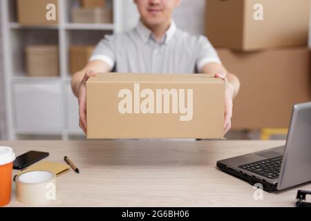 shipping and delivery concept - close up of young male postman giving parcel in post office Stock Photo