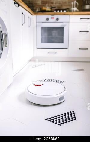 Robotic vacuum cleaner working on the kitchen floor. Stock Photo