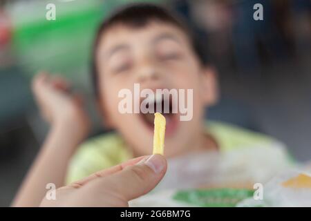 French fries in hand, fast food, in front of a hungry toddler. Stock Photo