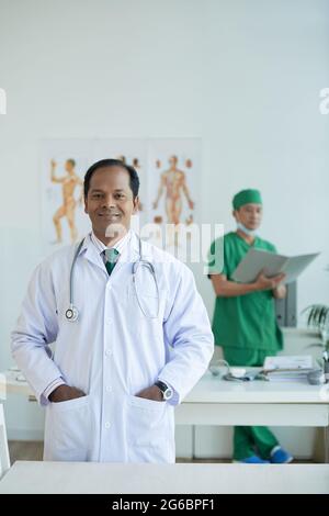 Portrait of smiling chief physician with stethoscope standing with hands in pockets Stock Photo