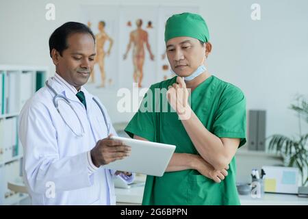 Pensive surgeon looking at patients x-ray on tablet computer in hands of chief physician Stock Photo