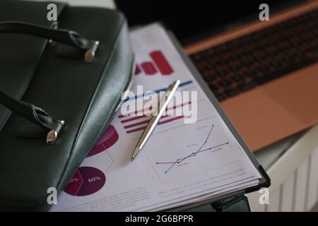 Clipboard documents and ballpoint pen lying on open green laptop bag closeup Stock Photo