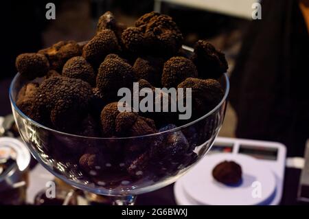 Italian black trouffles mushrooms in a glass bowl and a single trouffle mushroom on a weight scale in background Stock Photo