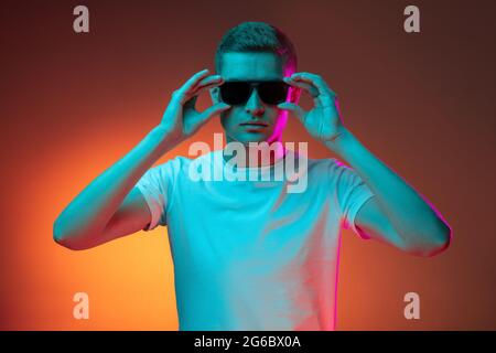 Portrait of young Caucasian man in casual clothes isolated over gradient red orange studio background in neon light with copyspace for ad. Concept of Stock Photo