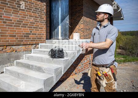 An electrician holds a construction drawing in his hands and inspects a working object. Stock Photo
