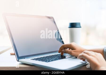 Person working with laptop and reusable coffee cup. Hands typing text on computer keyboard in the office, daylight. Technology and workplace concept Stock Photo