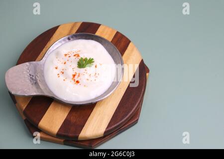 Fresh garlic dip yogurt sauce isolated on blue background. Spiced Curd garnished with coriander and spices. Dahi Raita. Copy space. Stock Photo