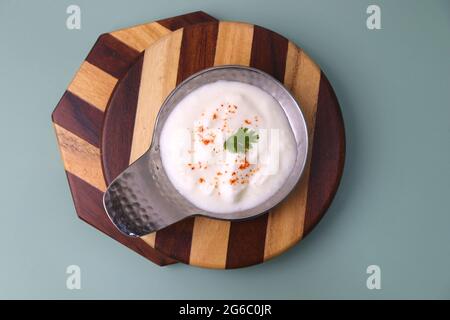 Fresh garlic dip yogurt sauce isolated on blue background. Spiced Curd garnished with coriander and spices. Dahi Raita. Copy space. Stock Photo