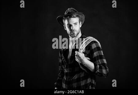 Western life. Lassoing on prairie. Man unshaven cowboy black background. Cowboy wearing hat hold rope. Lasso tool of American cowboy. Still used on Stock Photo