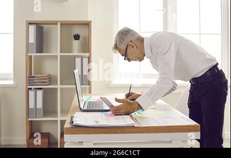 Serious focused busy senior businessman writes notes on colored sticky stickers. Stock Photo