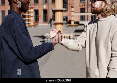 Side view portrait of two men greeting each other outdoors in city with focus on handshake Stock Photo