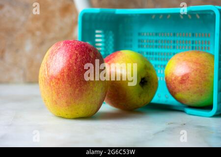 Close up of apples falling out of the plastic crate on a marble background. Stock Photo