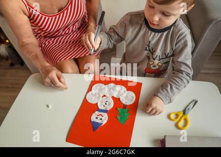 A Little boy with grandmother make Christmas craft, greeting card from cotton pads. Stock Photo