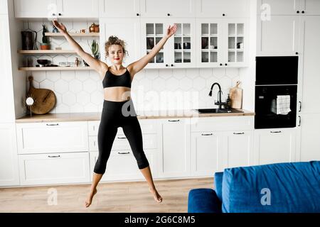 Silhouette of young cool attractive yoga woman practicing yoga, doing jumping exercise, raising hands, working out, wearing sportswear at home kitchen Stock Photo