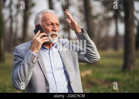 Senior businessman is talking on smartphone. He is upset. Stock Photo