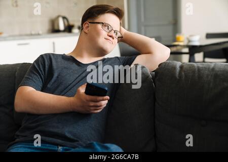 Young man with down syndrome using cellphone while sitting on couch at home Stock Photo