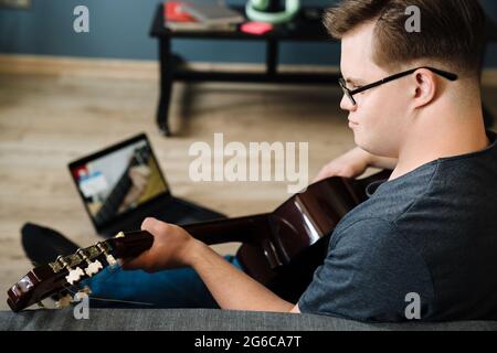 Young man with down syndrome playing guitar while using laptop at home Stock Photo