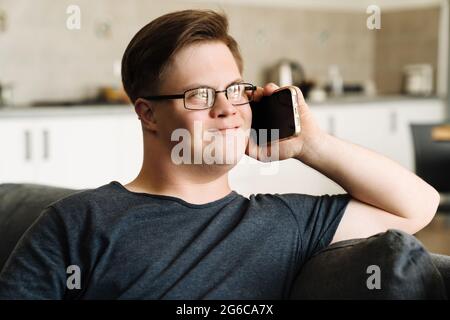 Young man with down syndrome talking on cellphone while sitting at home Stock Photo